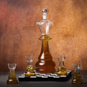 A crystal glass whiskey decanter shaped like a chess king piece, filled with amber liquor, surrounded by four matching shot glasses shaped like chess rook pieces, resting on a small black and white chessboard tray.