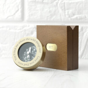 A polished brass compass engraved with the message 'You’ll find me where the wild things are! Love you Dad xxxx' resting next to a monogrammed wooden gift box with 'HT' engraved on a brass plate.