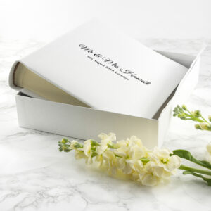 A white leather wedding photo album with Mr & Mrs Howell engraved on the cover, presented in a box with flowers.