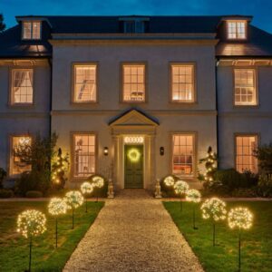 A twilight view of a grand house with an illuminated garden path. Multiple glowing, round dandelion-shaped solar lights are staked along both sides of the gravel walkway, emitting a warm white light against the dusk sky.