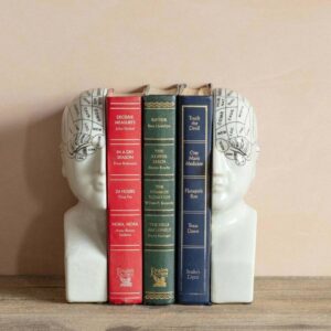 A pair of white, antiqued phrenology head bookends supporting a row of vintage-style books on a wooden surface.