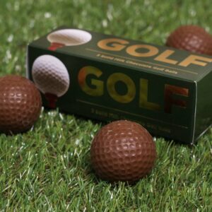 Close-up of solid milk chocolate golf balls sitting on artificial grass with a green gift box.