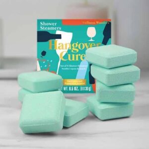 Set of 8 square green Hangover Cure Shower Steamers, scented with eucalyptus and peppermint, stacked next to the colorful 'Wellness Wonders' product box.