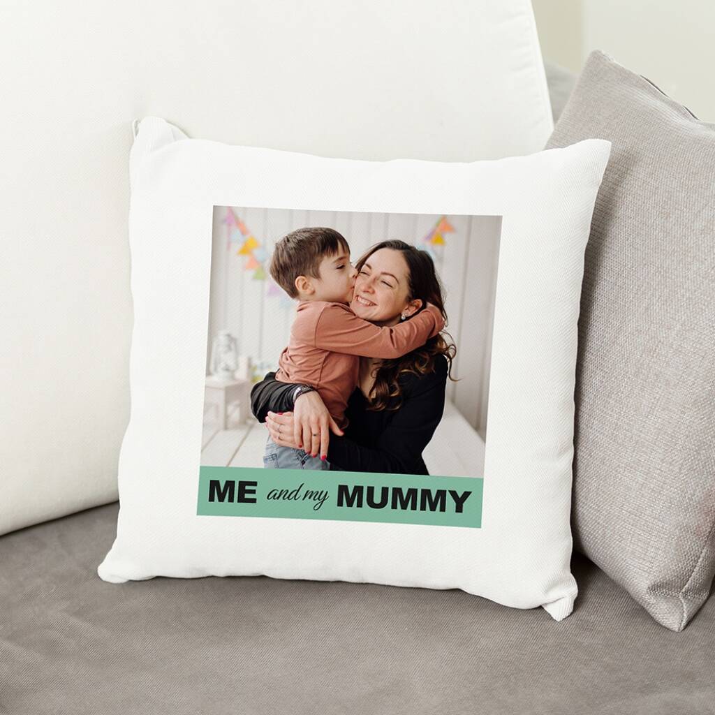 A square white cushion cover featuring a large printed photo of a happy woman (Mum) being hugged and kissed on the cheek by a young boy. Beneath the photo is a green banner with the text "ME and my MUMMY". The cushion is displayed on a grey sofa.