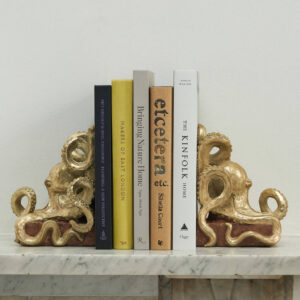 Pair of decorative antique gold-effect octopus bookends, featuring detailed tentacles wrapped around a brown base, holding five modern books upright on a white marble mantelpiece.
