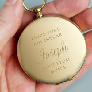 Close-up of a hand holding a highly polished, round, gold-toned keepsake compass engraved with a personalized message: 'Enjoy Your Adventure, Joseph, Love From Mum X'. Ideal personalised graduation, travel, or retirement gift.