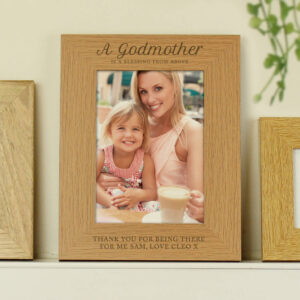 Personalised wooden photo frame engraved with the fixed text "A Godmother is a blessing from above" at the top and custom personalised text below the photo, currently showing "Thank You for being there for me Sam, Love Cleo x". The frame holds a 5x7 portrait photo of a smiling woman holding a little girl.