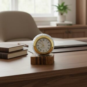 Desk clock featuring a golf ball casing and a gold-tone quartz face with Roman numerals, set on a wooden base.