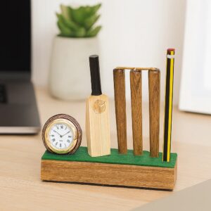 Wooden cricket-themed desktop organizer and clock set, featuring a miniature cricket ball clock, bat, and wicket stumps that serve as a pencil stand, set on a wooden desk with a green felt base.