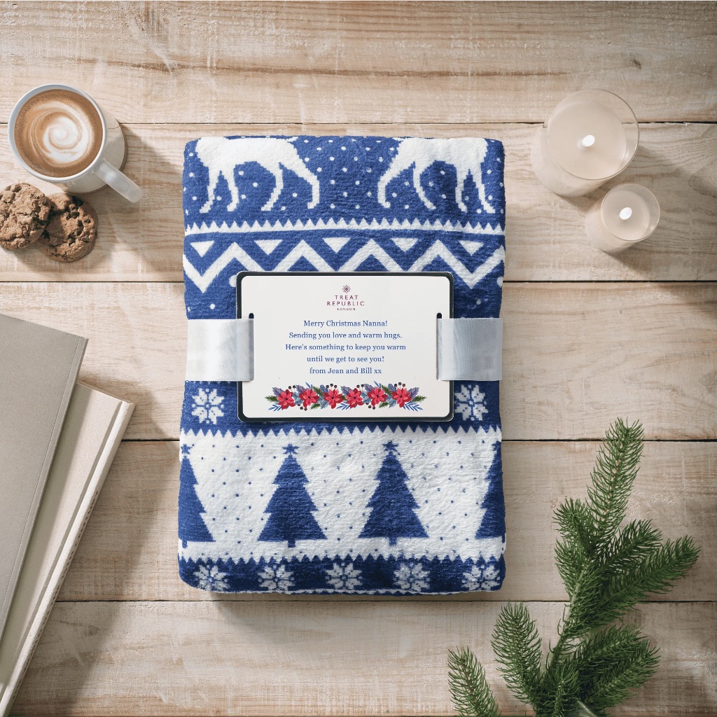 Personalised navy and white reindeer print fleece blanket, folded and tied with a ribbon, featuring a custom card message.