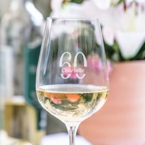 A large, stemmed wine glass filled with white or rosé wine, engraved with the large number '60' and the personalised name 'Charlotte' underneath, designed as a commemorative gift for a milestone birthday or anniversary.