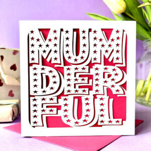 Alt Text: A luxury square Mother's Day card featuring the word "MUMDERFUL" in a bold, white laser-cut font with intricate star-shaped cut-outs, layered over a vibrant pink background with a matching pink envelope.