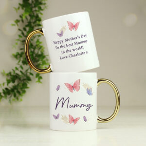 Two white ceramic mugs with elegant gold-plated handles, stacked on a white surface. The mugs feature a delicate butterfly and leaf design in pink and purple. One mug is personalised with "Mummy," and the other features a heartfelt message: "Happy Mother’s Day To the best Mummy in the world! Love Charlotte x."