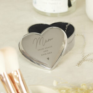 A luxury polished silver heart-shaped trinket box, shown open to reveal a dark velvet lining with a delicate silver chain inside. The lid is elegantly engraved with "Mum, From Grace and Evie xxx" and a small heart icon.