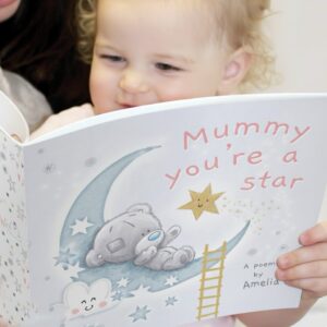A young child holding an open personalised 'Mummy You're A Star' poem book. The cover features an adorable Tiny Tatty Teddy sleeping on a crescent moon among stars and clouds, with the title in soft pink lettering.
