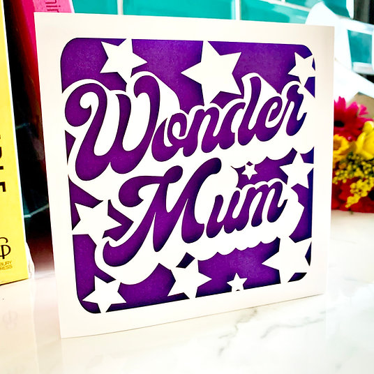 A luxury square Mother’s Day card featuring the words "Wonder Mum" in a bold, white cursive laser-cut font. The design is surrounded by white star cut-outs, all layered over a vibrant, textured purple background.