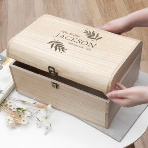 Personalised Wedding Date Keepsake Chest: A large Paulownia wood keepsake chest with a curved lid, engraved with "Mrs & Mrs Jackson" and a wedding date, being held by hands.