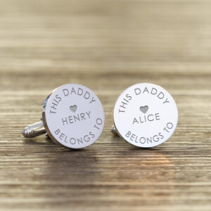 Pair of polished round silver cufflinks engraved with 'THIS DADDY BELONGS TO' and the names Henry and Alice, displayed on a textured wooden surface.