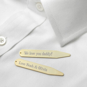 A pair of luxurious 18K gold-plated collar stiffeners lying on a crisp, pristine white dress shirt. The top stiffener is engraved with "We love you daddy!" and the bottom one with "Love Noah & Olivia" in an elegant, classic Serif font.