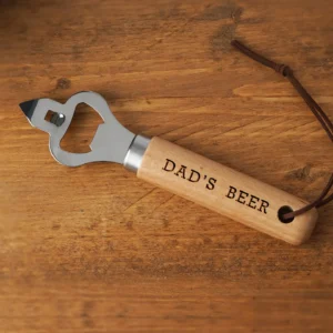 Engraved 'Dad's Beer' bottle opener with a natural wooden handle and stainless steel opener tip, resting on a rustic wooden table.