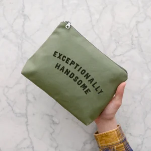 A person holding a rectangular olive green canvas wash bag against a white marble background. The bag has the text "EXCEPTIONALLY HANDSOME" printed in dark green on the front, with a visible matt silver metal zip at the top.