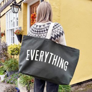 A person wearing a smart grey canvas tote bag with 'EVERYTHING' printed in large white letters, standing in front of a yellow building.