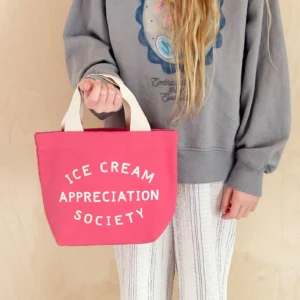 A person wearing a grey sweater holding a small, bright pink canvas tote bag that reads 'Ice Cream Appreciation Society' in white text.