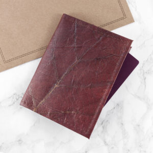 A rich, earthy brown Leaf Leather Passport Cover with visible leaf vein textures, resting on a white marble surface next to a neutral kraft paper envelope.