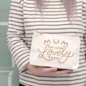 A person wearing a cream and brown striped long-sleeved top holding a natural canvas make-up bag with the words "Mum, You Look Lovely Today" printed in metallic gold lettering.