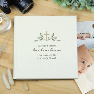 A cream-coloured, square-bound photo album cover featuring a printed cross design and green botanical sprigs. The text on the cover reads "On Your Baptism," "Amelia Rose," "22nd August 2024," and "St Peter's Church".
