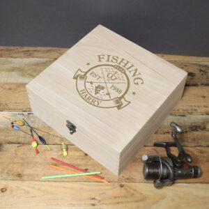 Personalised Fishing Club Keepsake Box: A large, square wooden keepsake box with a metal clasp, featuring an engraved "Fishing Club" logo with a fish and hooks design. The box is personalised with "EST. 1988" and the name "HARRY." It is displayed on a wooden surface next to a fishing reel and several colourful fishing floats.