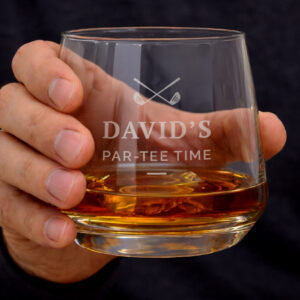 A hand holding a personalized glass whiskey tumbler filled with amber liquid and ice, featuring an engraved golf club logo and text that reads "David's Par-Tee Time."
