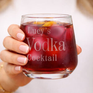 Personalised Favourite Drink Tumbler: A hand holding a custom-engraved glass tumbler filled with a dark red vodka cocktail and ice. The engraving reads "Lucy's Vodka Cocktail" in a sophisticated serif font.