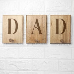 Personalised solid oak wall hook mounted on a white brick background, featuring an engraved letter "D" and "A" and "D" on a three minimalist wooden peg.