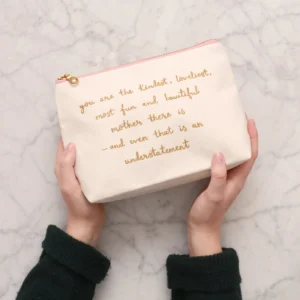 A pair of hands holding a natural cream-coloured canvas make-up bag, featuring metallic gold text that reads: "you are the kindest, loveliest, most fun and beautiful mother there is - and even that is an understatement"