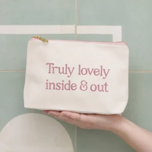 A pair of hands holding a natural canvas make-up bag against a sage green tiled wall, with the text "Truly lovely inside & out" printed in pink lettering.