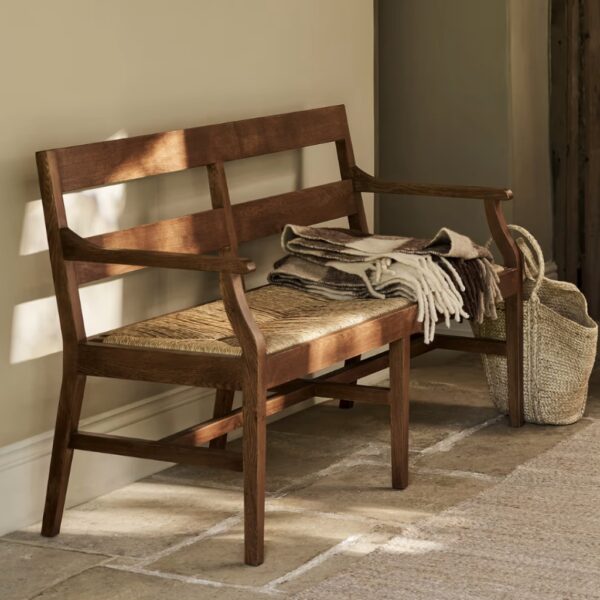 Dark oak wooden bench with woven seagrass seat in a sunlit hallway with folded throw blanket