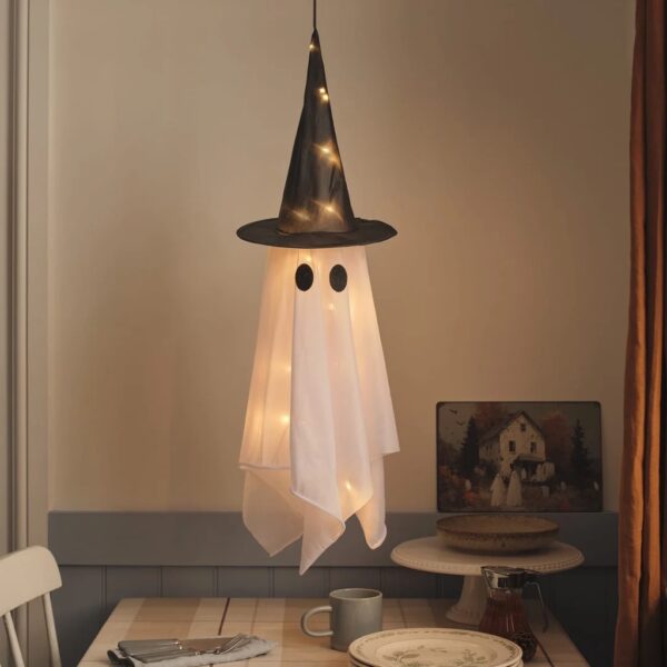 Light-up hanging witch ghost Halloween decoration with black hat floating above a dining table with warm LED lights