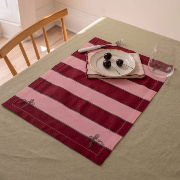 Set of 2 cotton placemats in bold pink and burgundy stripes with embroidered bow motifs on a sage green tablecloth