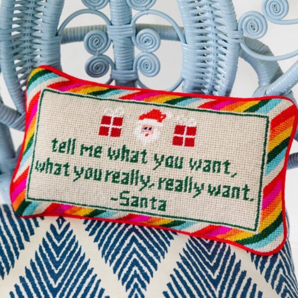 'Tell Me What You Want' hand-stitched needlepoint Christmas cushion displayed on a blue woven armchair